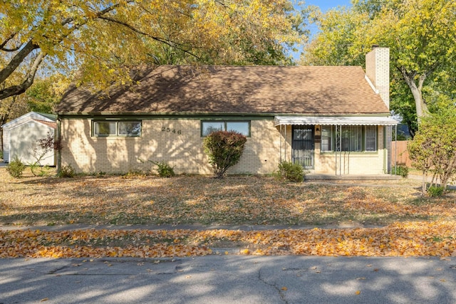 ranch-style home featuring brick siding, a chimney, and roof with shingles