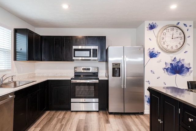 kitchen featuring dark cabinetry, a sink, stainless steel appliances, light countertops, and light wood-style floors