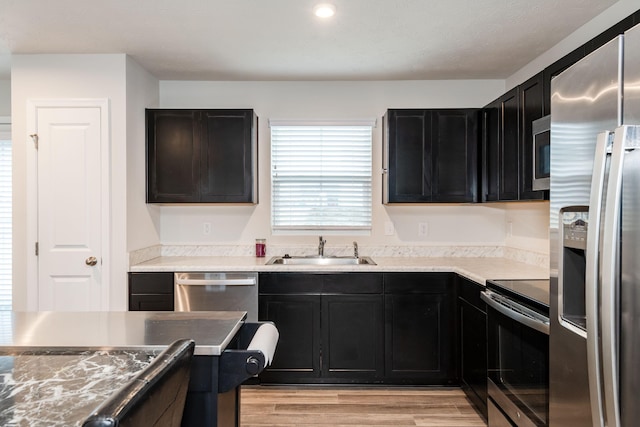 kitchen with a sink, light wood-style flooring, appliances with stainless steel finishes, and dark cabinets