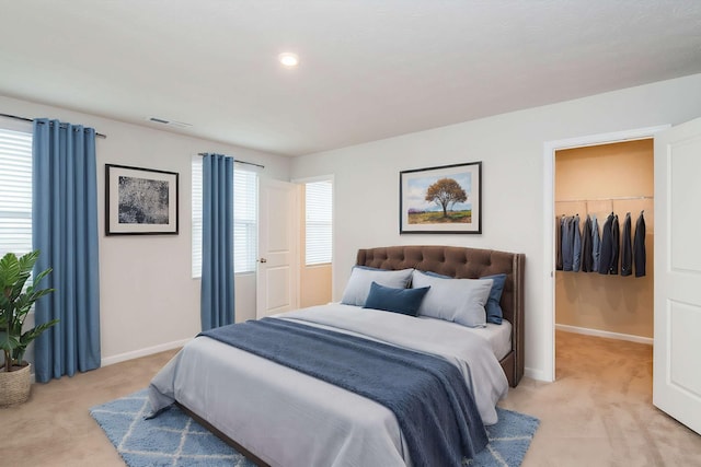 bedroom with a spacious closet, visible vents, light carpet, and baseboards