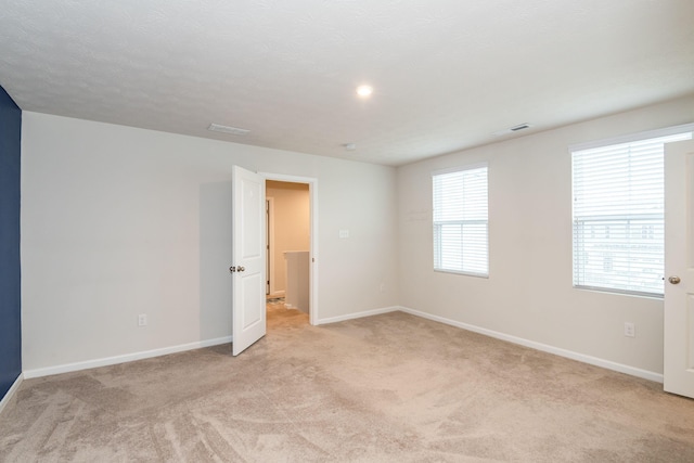 unfurnished room with light carpet, visible vents, and baseboards