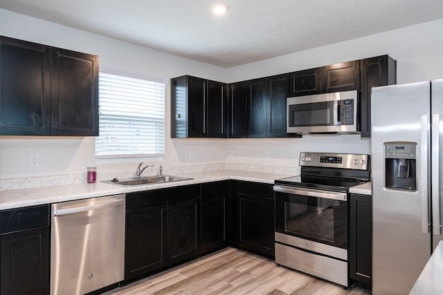 kitchen featuring light wood finished floors, appliances with stainless steel finishes, dark cabinetry, and a sink