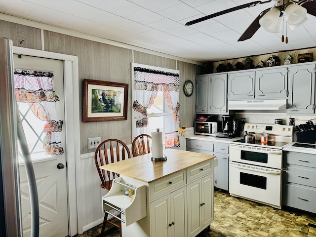 kitchen with range with two ovens, a wealth of natural light, ceiling fan, and wood walls