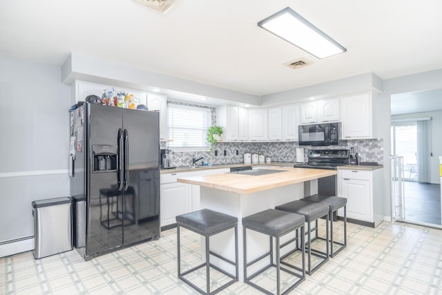 kitchen with visible vents, black appliances, a kitchen breakfast bar, wooden counters, and light floors