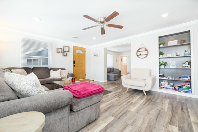 living room featuring ceiling fan, built in shelves, baseboards, light wood-type flooring, and crown molding