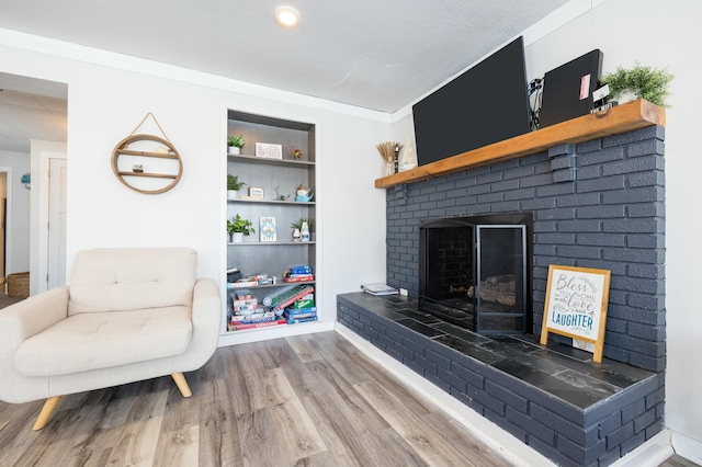 living area featuring built in features, a fireplace, ornamental molding, wood finished floors, and baseboards