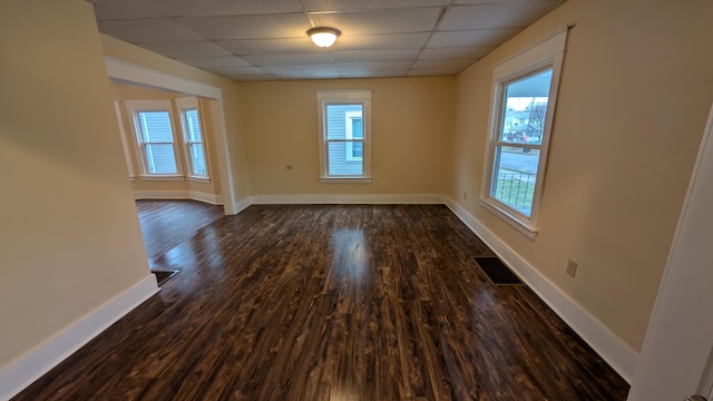 unfurnished room with a wealth of natural light, a drop ceiling, and dark hardwood / wood-style flooring