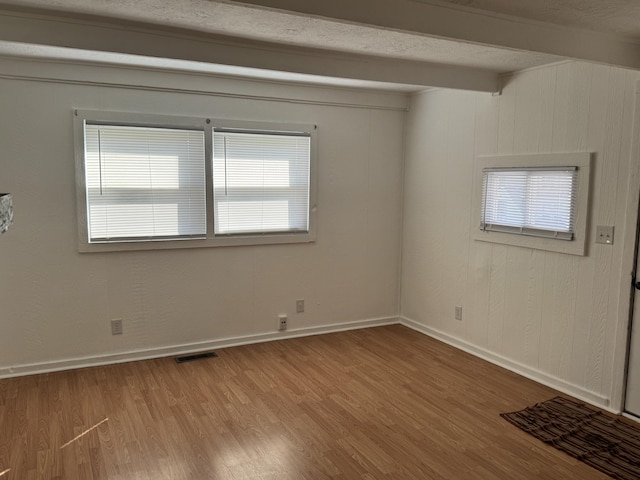 spare room featuring baseboards, visible vents, wood finished floors, beamed ceiling, and a textured ceiling