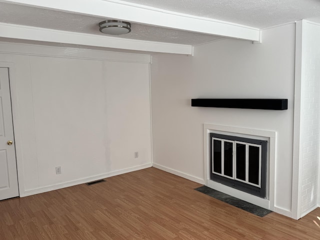 unfurnished living room featuring a textured ceiling, wood finished floors, a fireplace with flush hearth, visible vents, and beamed ceiling