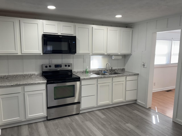 kitchen with black microwave, a sink, white cabinets, stainless steel electric stove, and light wood finished floors