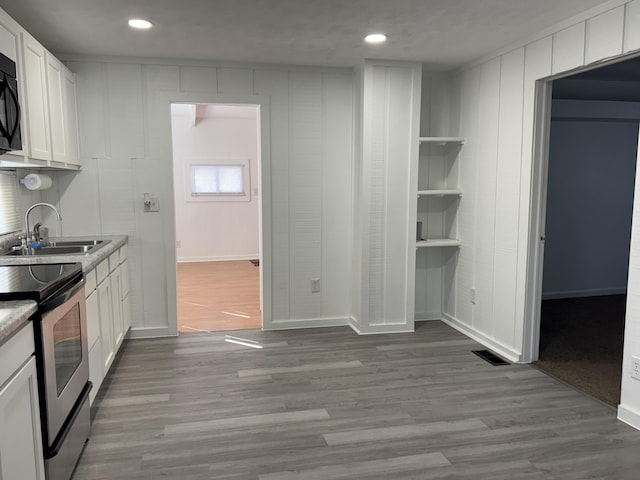 kitchen with black microwave, a sink, wood finished floors, white cabinets, and stainless steel range with electric stovetop