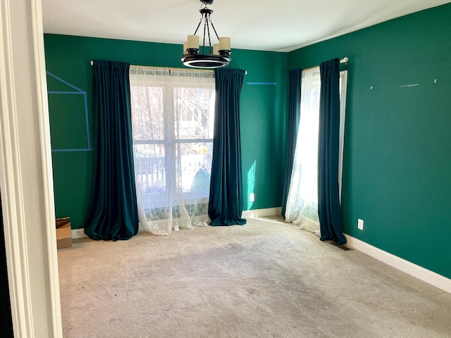 empty room with a notable chandelier, carpet flooring, and baseboards