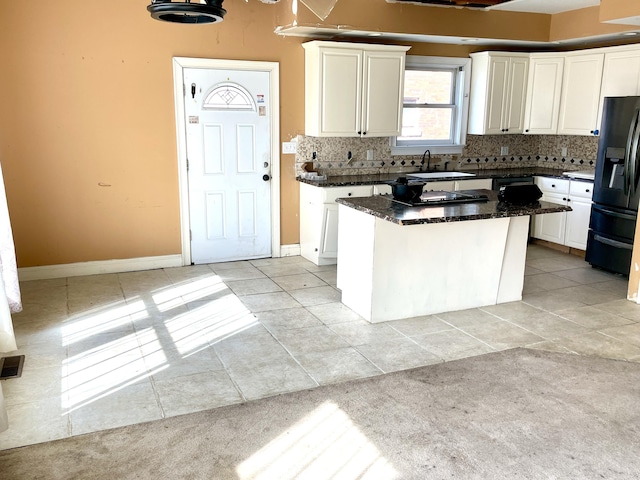 kitchen featuring light tile patterned floors, backsplash, white cabinets, and black refrigerator with ice dispenser