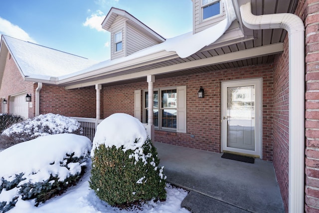 snow covered property entrance featuring brick siding and a porch