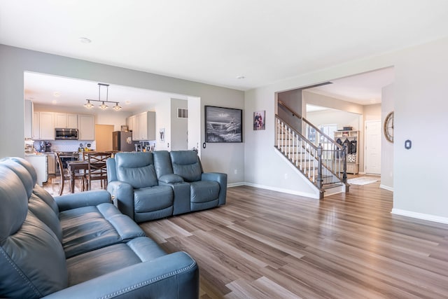 living area featuring baseboards, light wood-type flooring, visible vents, and stairs