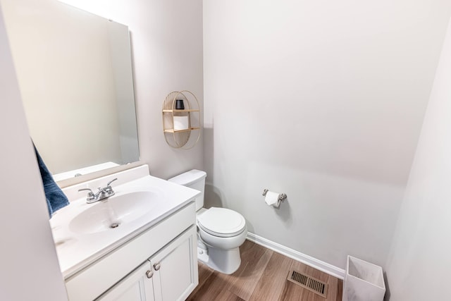 bathroom with vanity, toilet, visible vents, baseboards, and wood finished floors