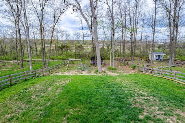 view of yard with a trampoline, fence, and an outbuilding