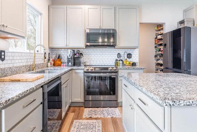 kitchen with tasteful backsplash, light stone counters, light wood-style floors, appliances with stainless steel finishes, and a sink