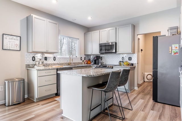 kitchen featuring a kitchen breakfast bar, light wood-style flooring, a sink, appliances with stainless steel finishes, and backsplash