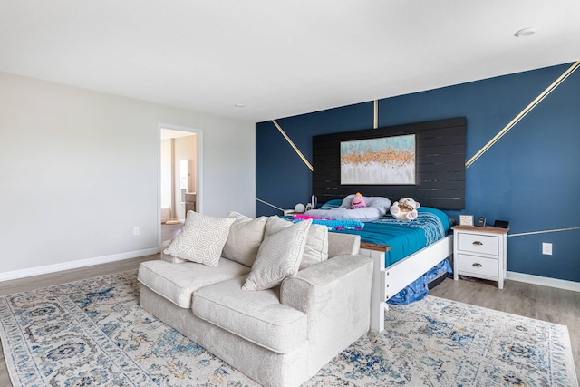 bedroom with connected bathroom, wood finished floors, and baseboards