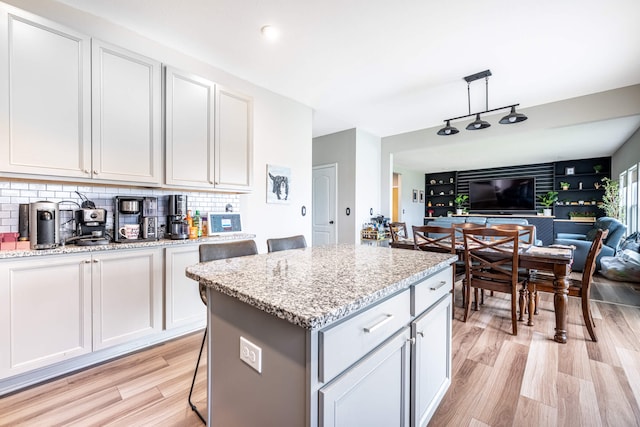 kitchen with decorative backsplash, light wood-style floors, light stone counters, white cabinets, and open floor plan