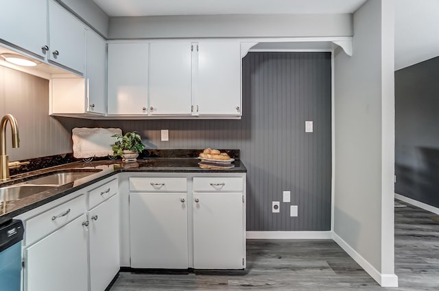 kitchen featuring dishwashing machine, wood finished floors, a sink, and white cabinetry