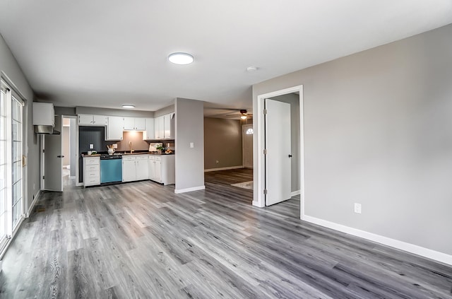 kitchen with dishwashing machine, dark countertops, white cabinetry, light wood-type flooring, and baseboards