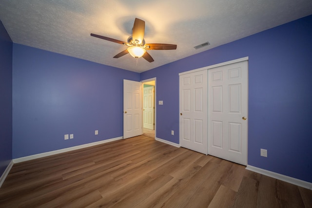 unfurnished bedroom with ceiling fan, a closet, hardwood / wood-style floors, and a textured ceiling