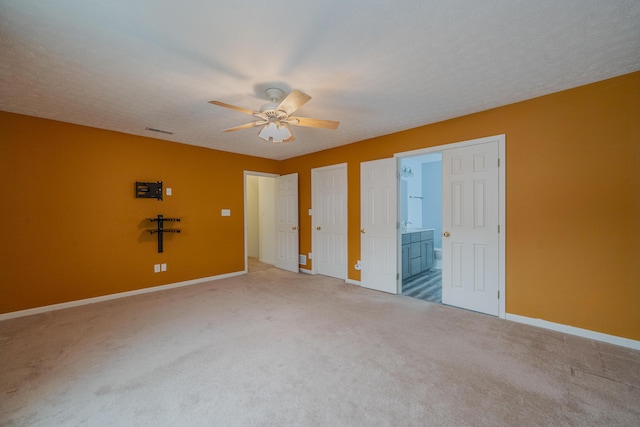 unfurnished bedroom with ceiling fan, carpet flooring, a textured ceiling, and ensuite bath