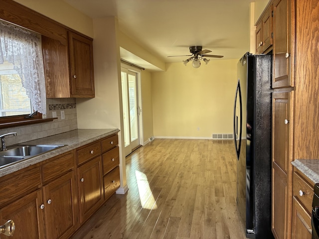 kitchen featuring brown cabinetry, visible vents, light wood finished floors, and freestanding refrigerator