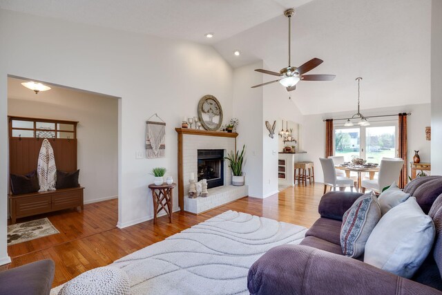 living room with a ceiling fan, a fireplace, wood finished floors, high vaulted ceiling, and baseboards