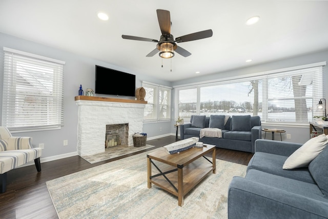 living area with a stone fireplace, recessed lighting, wood finished floors, a ceiling fan, and baseboards