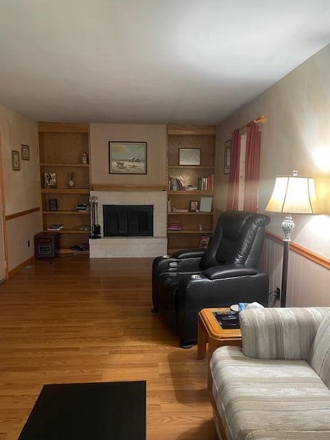 living area featuring light wood-style floors, wainscoting, and a fireplace with raised hearth