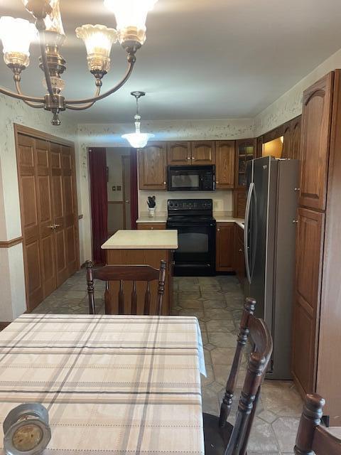kitchen with brown cabinetry, an inviting chandelier, a kitchen island, black appliances, and light countertops