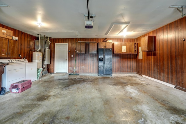 garage featuring washing machine and clothes dryer, black fridge with ice dispenser, wood walls, and a garage door opener