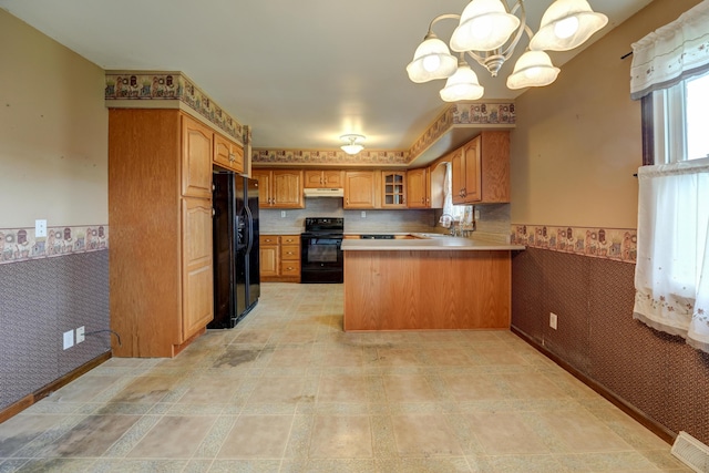 kitchen with a wainscoted wall, a peninsula, under cabinet range hood, wallpapered walls, and black appliances