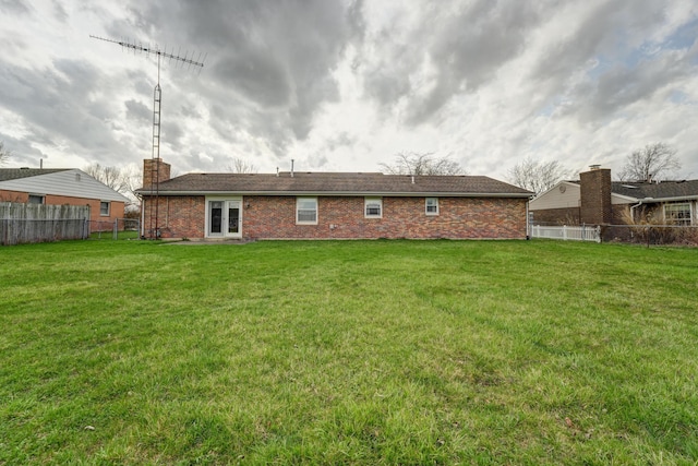 back of property with brick siding, fence, a yard, and a chimney