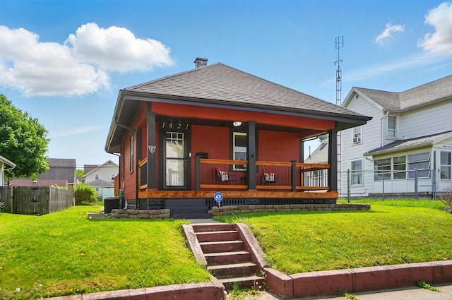 back of property featuring covered porch, a lawn, a chimney, and roof with shingles