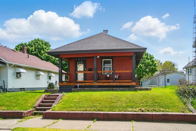 view of front facade featuring roof with shingles, covered porch, and a front yard