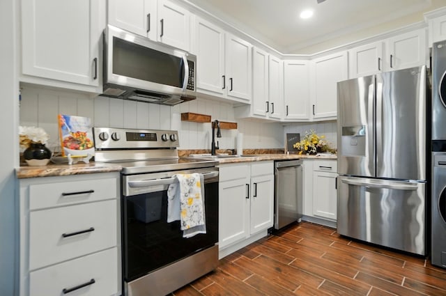 kitchen with white cabinets, stainless steel appliances, a sink, and stacked washer / dryer