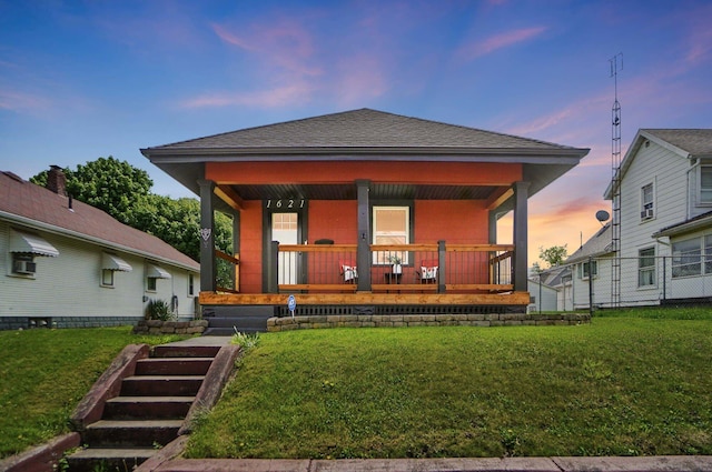 back of house featuring a porch, a lawn, roof with shingles, and fence