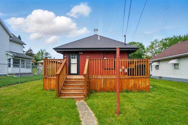 back of property with a lawn, roof with shingles, and a deck
