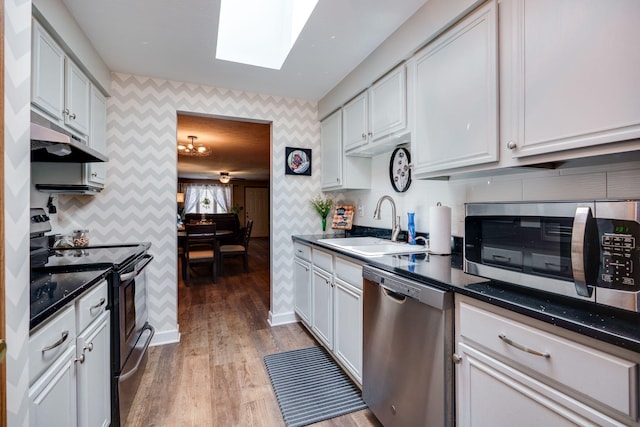 4212 Midfield St, Springfield, OH 45503 - kitchen with wallpapered walls, stainless steel appliances, a skylight, under cabinet range hood, and light wood-style flooring