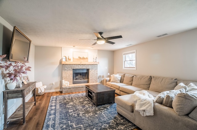 living room featuring ceiling fan, a fireplace, dark hardwood / wood-style flooring, and a textured ceiling