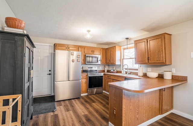 kitchen with sink, dark wood-type flooring, appliances with stainless steel finishes, decorative light fixtures, and kitchen peninsula