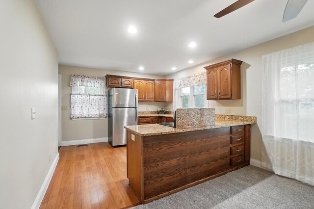 kitchen featuring freestanding refrigerator, a peninsula, light stone counters, a ceiling fan, and baseboards