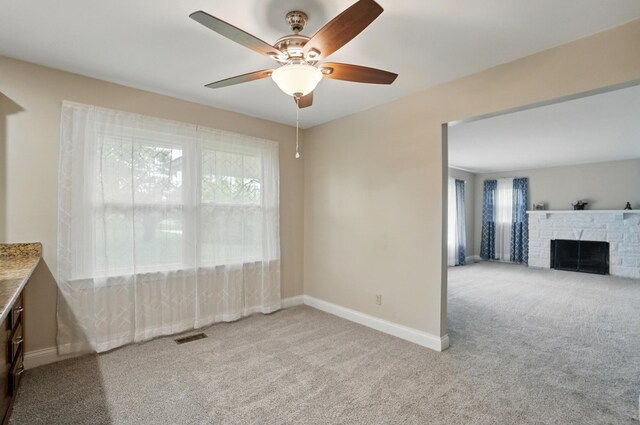 carpeted empty room featuring healthy amount of natural light, a ceiling fan, baseboards, and a stone fireplace