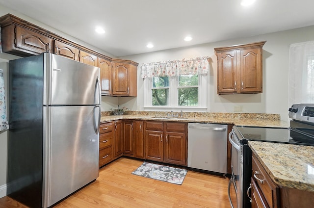 kitchen with appliances with stainless steel finishes, a sink, light stone counters, light wood-style floors, and recessed lighting