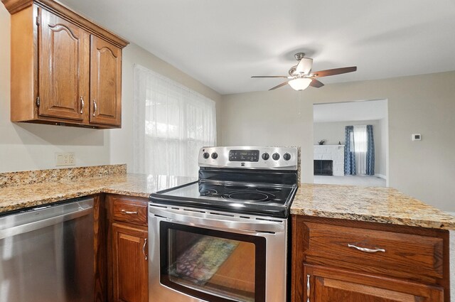 kitchen featuring stainless steel appliances, a ceiling fan, brown cabinetry, a peninsula, and a fireplace