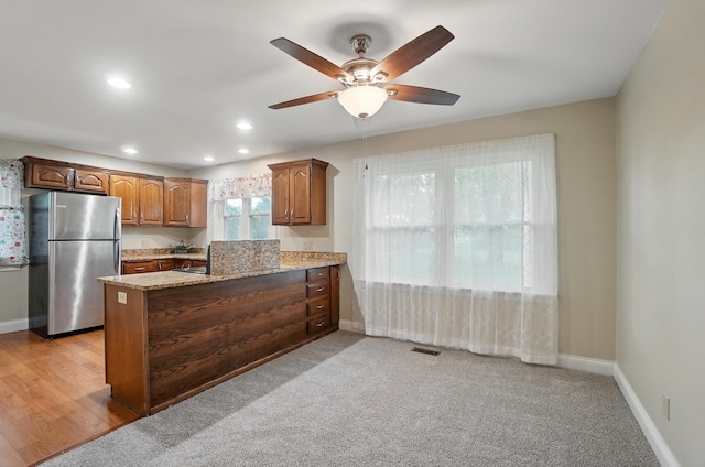 kitchen with freestanding refrigerator, light stone countertops, a peninsula, a ceiling fan, and baseboards